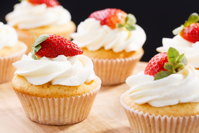 Muffinki z bita śmietaną i kawałkiem truskawki na wierzchu